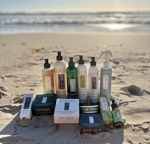 Collection of hair care products on a sandy beach with ocean in the background