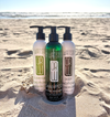 Three bottles of Dr. Watson hair care products on a sandy beach.