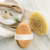 Wooden brush with natural bristles on a marble surface with a towel and plant.